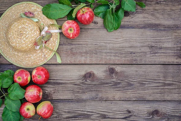 Red apples and straw hat on wooden background