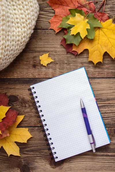 Autumn picture with a notebook and pen, yellow leaves and scarf on wooden background — Stock Photo, Image