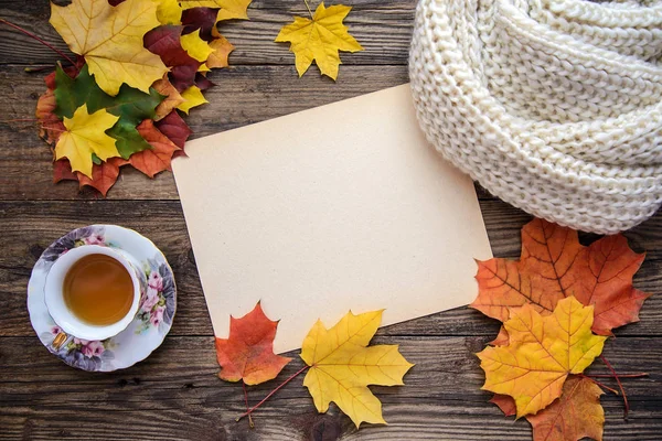 Sarı yapraklar, bir bardak çay, bir eşarp ve Kağıt ahşap arka plan üzerinde sonbahar resim — Stok fotoğraf