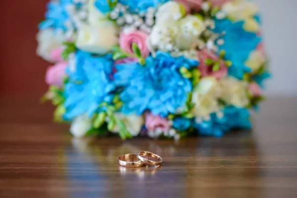 Engagement rings and wedding bouquet on a wooden table — Stock Photo, Image