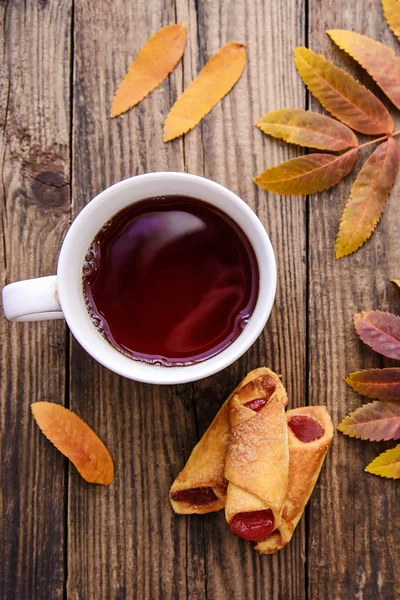 Autumn picture of yellow leaves, a cup of tea, a scarf and a piece of paper with pen on wooden background with cookies