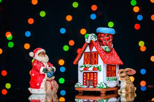 Рождественская фотография с Сантой и кроликом рядом с домом на фоне цветных огней — стоковое фото