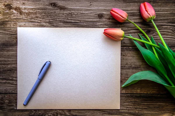 Three red Tulip and a piece of paper with a pen on a brown woode — Stock Photo, Image