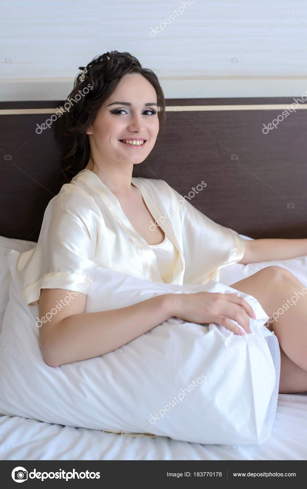 Beautiful Young Girl Sitting In Bed With White Pillow And Smiling