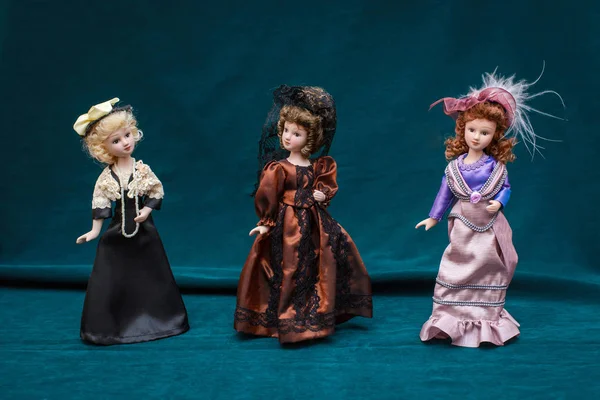 Three dolls in classic vintage dresses and hats on dark background — Stock Photo, Image