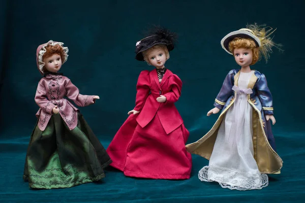 Three dolls in classic vintage dresses and hats on dark background — Stock Photo, Image