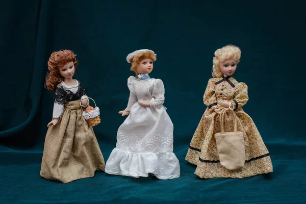 Three dolls in classic vintage dresses and hats on dark background — Stock Photo, Image