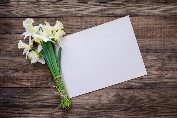 Bouquet of white with yellow daffodils and sheet of paper for writing on wooden background — Stock Photo, Image