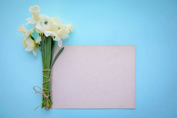 Daffodils on blue background with a piece of paper with copy space — Stock Photo, Image