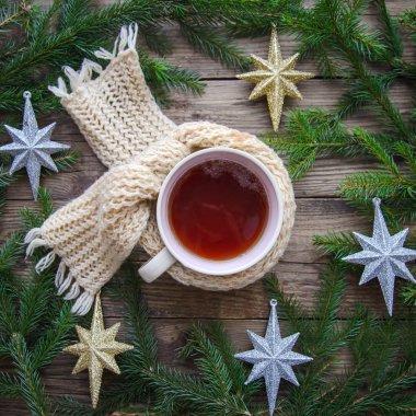 Bir kupa çay örülmüş bir eşarp içinde ahşap bir arka planda Noel yıldızlarıyla