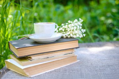 Bahar çiçekleri vadideki zambaklar ve eski kitapların üzerinde bir fincan çay.