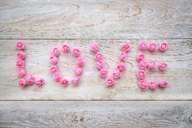 Tahta bir arka planda küçük pembe güllerden gelen aşk kelimesi