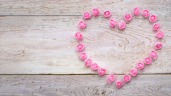 Серце з маленьких рожевих троянд на дерев'яному фоні — стокове фото