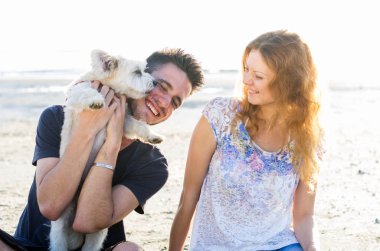 Aşk dolu çift deniz kenarında köpekle yürüyor.