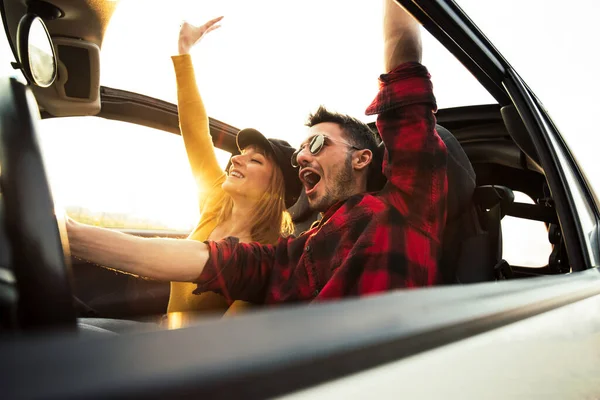 Happy couple driving a convertible car at sunset on the road