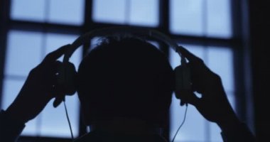 Bir genç çekici adam giyen kulaklık pencere akşam ağır çekim sahne. Müzik dinleme. 4k Uhd 4096 x 2160.