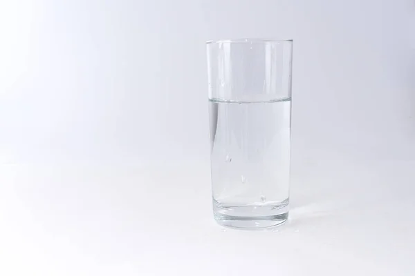 Wody pitnej przelewa się do szklanki na jasnym tle — Zdjęcie stockowe