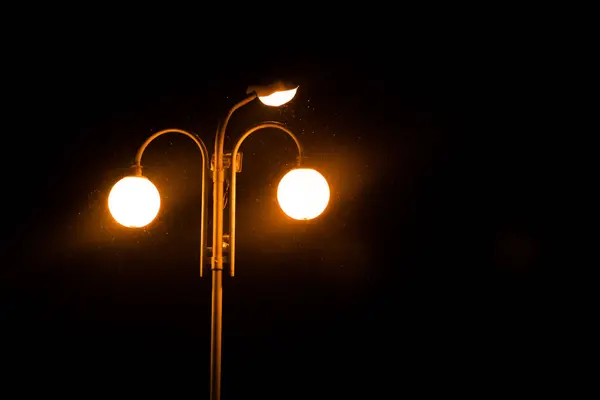 Uma lanterna acesa em um poste, no escuro — Fotografia de Stock
