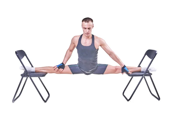 A handsome man performs a transverse twine, in sportswear on chairs isolated on a white background — Stock Photo, Image