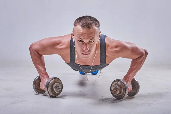 Een knappe sport man wordt uit de vloer met halters in zijn handen geperst — Stockfoto