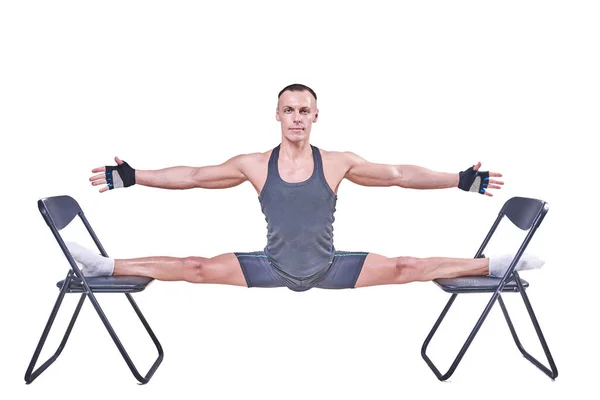 Un hombre guapo realiza un corte transversal, en ropa deportiva sobre sillas aisladas sobre un fondo blanco — Foto de Stock