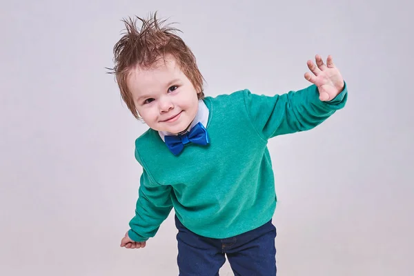 Красивый маленький мальчик в голубой бабочке и зеленом свитере, танцует и улыбается. — стоковое фото