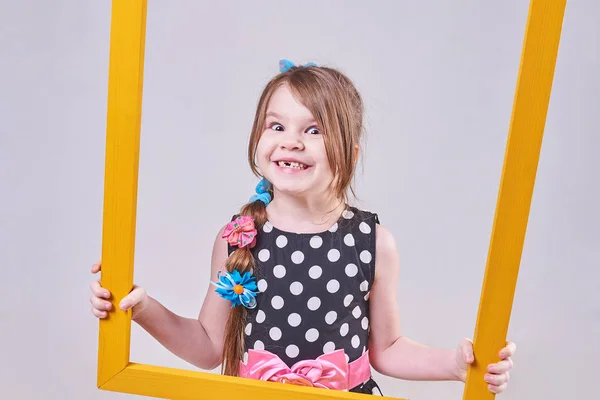 Menina bonita, com uma expressão engraçada em seu rosto, segurando uma moldura amarela — Fotografia de Stock