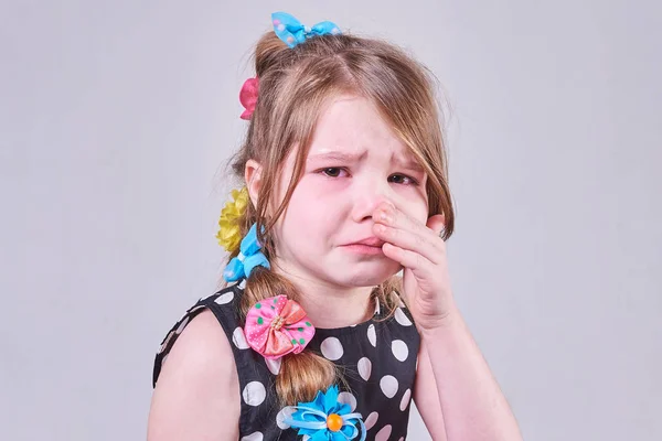 Uma menina bonita, com uma expressão triste, chora e enxuga as lágrimas com as mãos — Fotografia de Stock