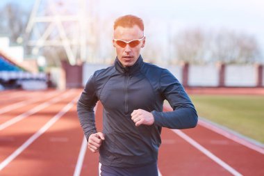 Koşu bandı stadyum üzerinde çalışan yakışıklı atletik erkek