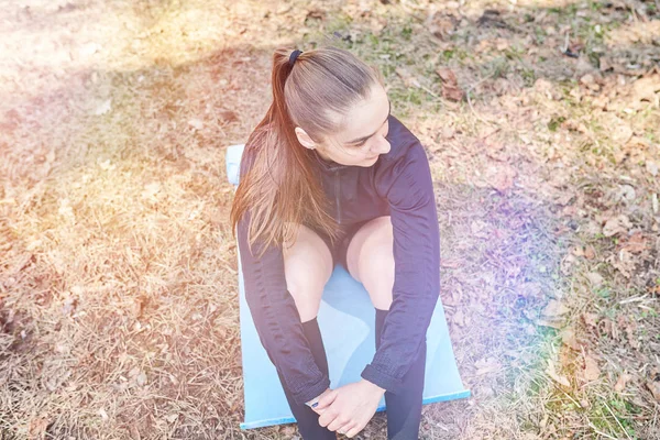 Sportig tjej sitter på en matta i skogen — Stockfoto