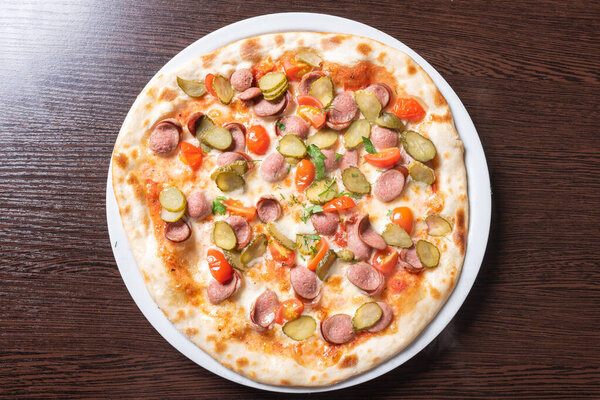 Cheap pizza with sausages, cucumbers, cherry tomatoes, and herbs.