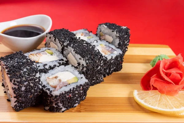 Sushi, rollos de sésamo negro, con queso, camarones y cangrejo. En el tablón. Sobre un fondo rojo . — Foto de Stock