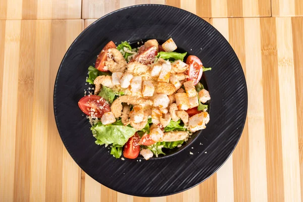Caesar-Salat auf schwarzem Teller, auf hölzernem Hintergrund. — Stockfoto