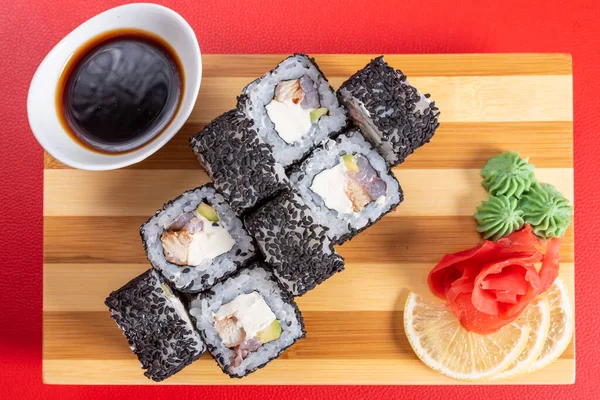 Sushi, rolos em gergelim preto, com queijo, camarão e caranguejo. Na prancha. Em um fundo vermelho . — Fotografia de Stock