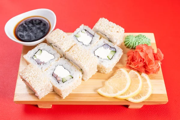 Sushi, rollos de sésamo blanco, con queso, aguacate y camarones. En el tablón. Sobre un fondo rojo . — Foto de Stock
