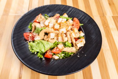 Siyah bir tabakta, ahşap bir zeminde Sezar salatası..