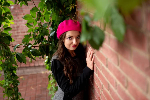 Ein Mädchen mit rosa Baskenmütze steht an einer Ziegelmauer. — Stockfoto