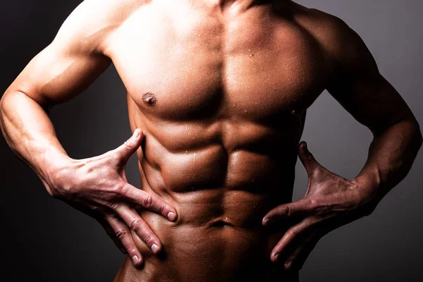 Beautiful, athletic, male torso. In contrast lighting. A man holds his hands near the press. — Stock Photo, Image