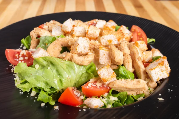Caesar-Salat auf schwarzem Teller, auf hölzernem Hintergrund. — Stockfoto