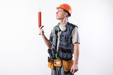 Miğferli bir müteahhit, silikonlu bir montaj silahı. El ele tutuşuyorlar. Hafif bir arkaplanda.