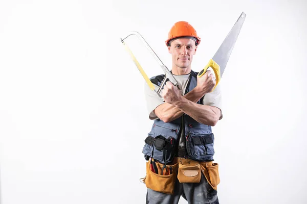 Un constructor con sierra en un casco, sonriendo. Sobre un fondo claro . — Foto de Stock