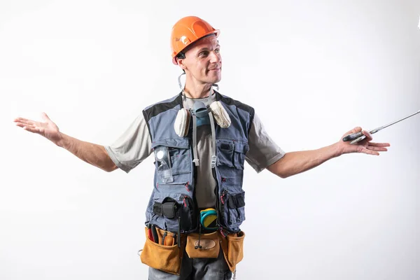 El constructor en un casco, y descargando, sostiene una sierra en sus manos en un árbol. Sobre un fondo claro . —  Fotos de Stock