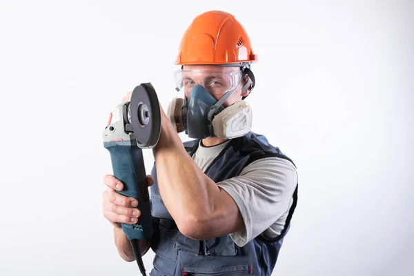 Construtor em um capacete e um respirador, com um moedor de ângulo em suas mãos . — Fotografia de Stock