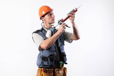 Miğferli bir müteahhit, silikonlu bir montaj silahı. El ele tutuşuyorlar. Hafif bir arkaplanda.