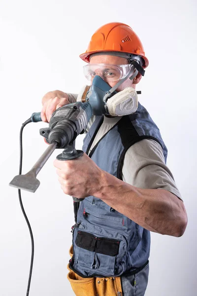 Construtor com um perfurador, em um capacete e um respirador . — Fotografia de Stock