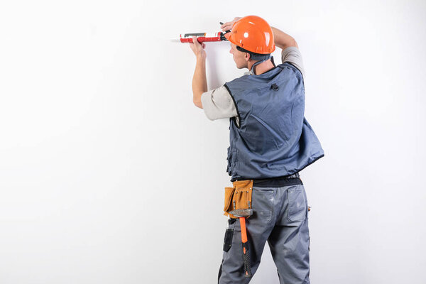 A builder in a helmet, with silicone in a mounting gun, aims at the frame.