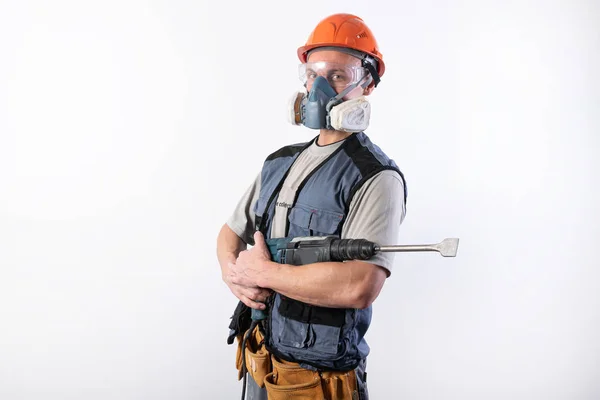 Construtor com um perfurador, em um capacete e um respirador. Fica com o dispositivo em suas mãos . — Fotografia de Stock