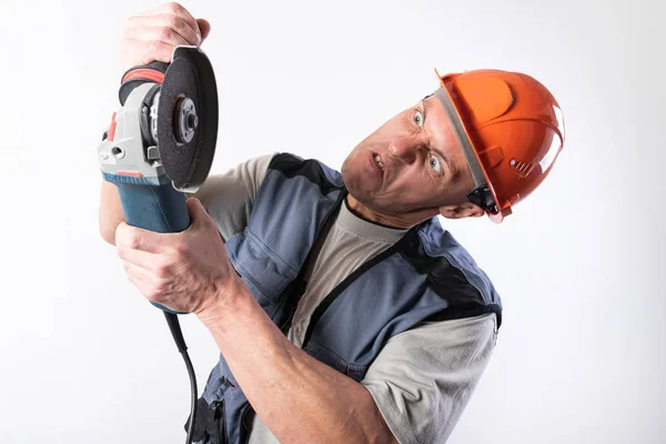 Construtor com moedor de ângulo, em um capacete, com uma expressão engraçada em seu rosto . — Fotografia de Stock