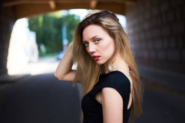 Siyah elbiseli seksi sarışın kız. Saplar ve çerçeveye bakar.