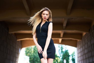 Siyah kısa elbiseli sarışın kız. Saçları uzamış. Köprünün altındaki kemerde.